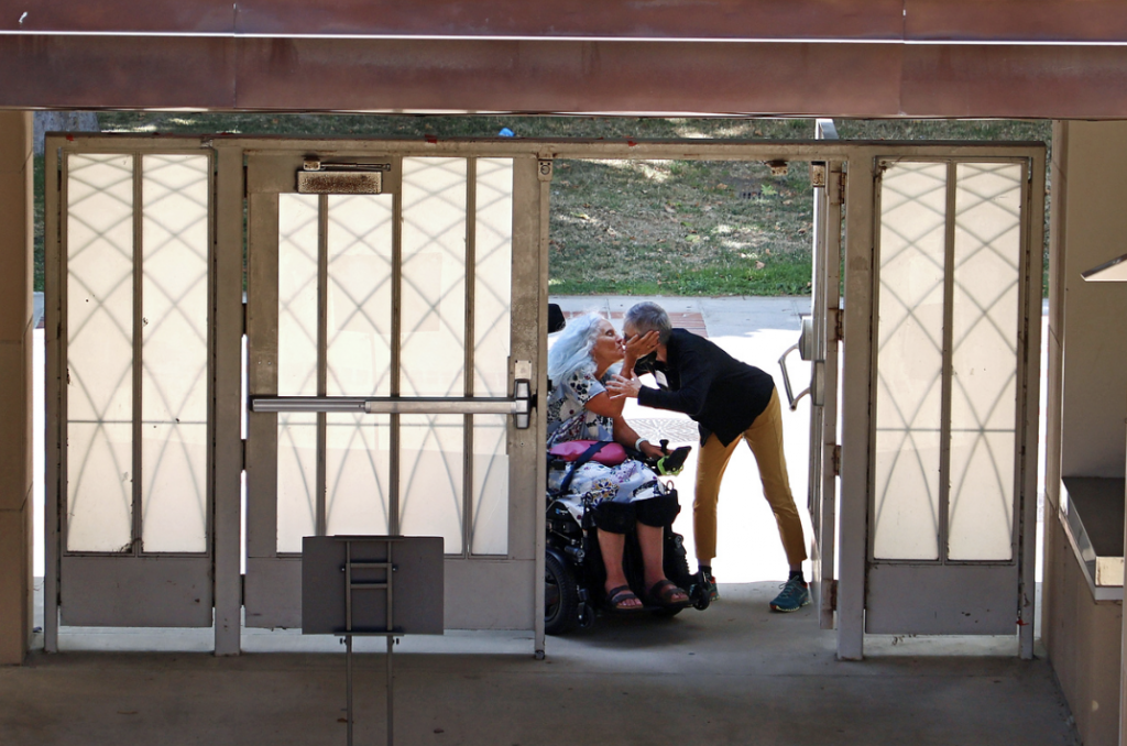 Two individuals, one of whom is using a wheelchair, embrace in a doorway.